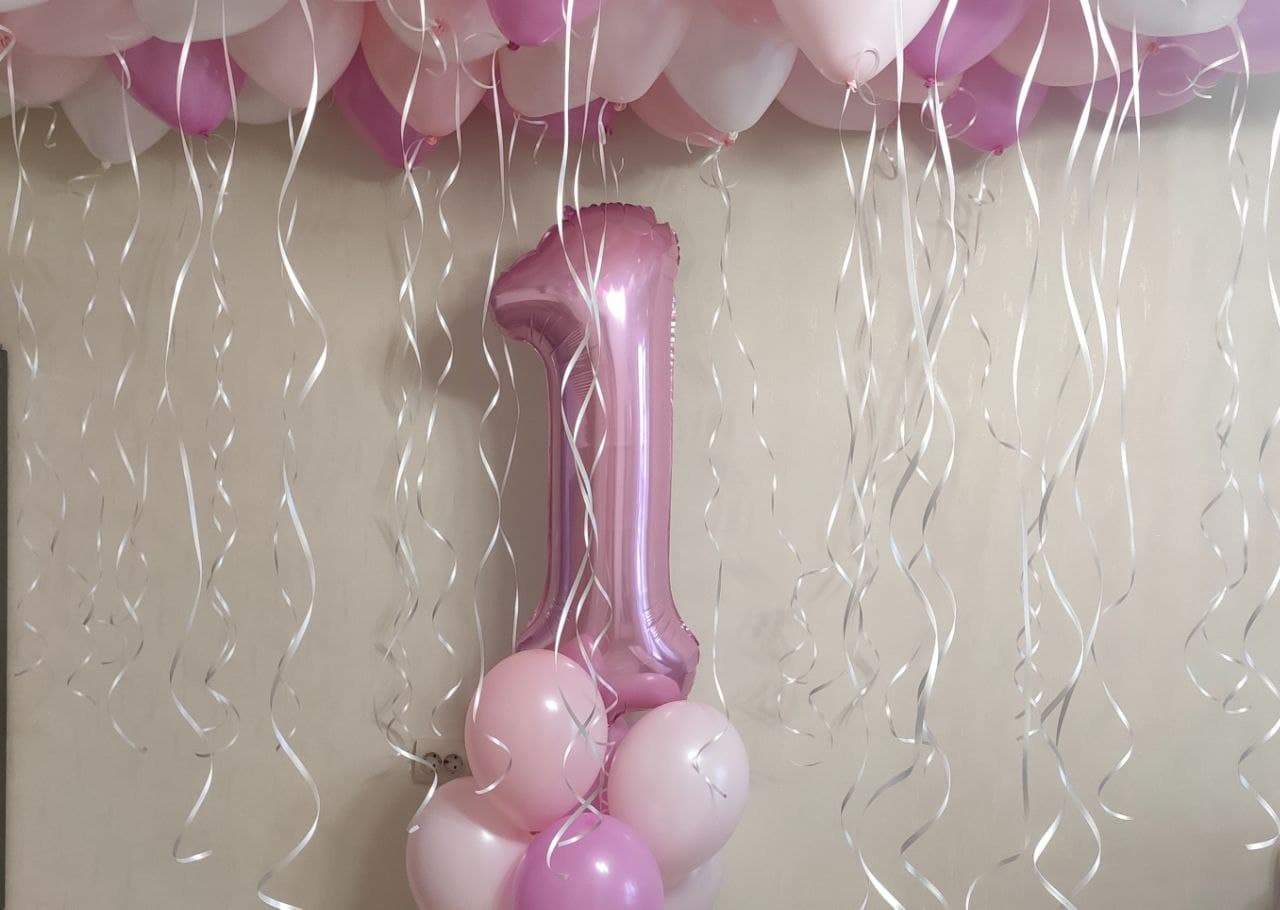 Композиция из гелиевых розовых шаров на годик девочке разных оттенков с цифрой один из фольги розового цвета и пудровые розовые и белые шарики с гелием под потолок с перламутровыми белыми ленточками.